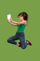 Image showing Image of young woman over green background using laptop computer or tablet gadget while jumping.