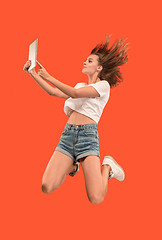 Image showing Image of young woman over red background using laptop computer or tablet gadget while jumping.