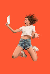 Image showing Image of young woman over red background using laptop computer or tablet gadget while jumping.