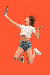 Image showing Image of young woman over red background using laptop computer or tablet gadget while jumping.