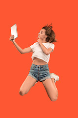 Image showing Image of young woman over red background using laptop computer or tablet gadget while jumping.