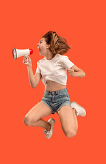 Image showing Beautiful young woman jumping with megaphone isolated over red background