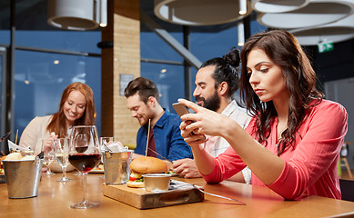 Image showing bored woman messaging on smartphone at restaurant