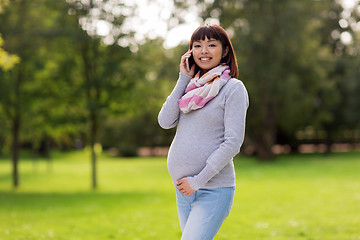 Image showing pregnant asian woman calling on smartphone at park