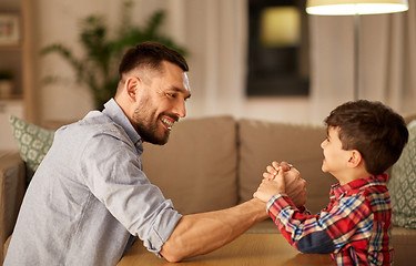 Image showing happy father and little son arm wrestling at home