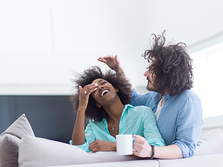 Image showing multiethnic couple sitting on sofa at home drinking coffe