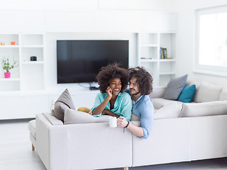 Image showing multiethnic couple sitting on sofa at home drinking coffe