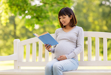 Image showing happy pregnant asian woman reading book at park