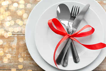 Image showing cutlery tied with red ribbon on set of plates