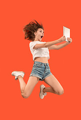 Image showing Image of young woman over red background using laptop computer or tablet gadget while jumping.