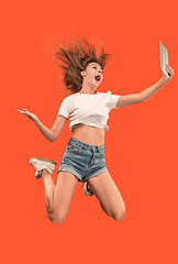Image showing Image of young woman over red background using laptop computer or tablet gadget while jumping.