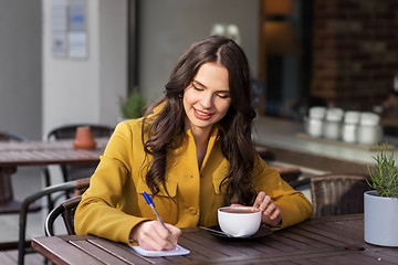 Image showing happy woman with notebook drinking cocoa at cafe