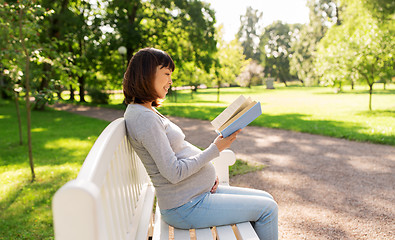 Image showing happy pregnant asian woman reading book at park