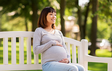 Image showing happy pregnant asian woman sitting on park bench