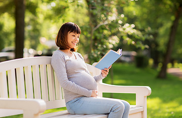 Image showing happy pregnant asian woman reading book at park