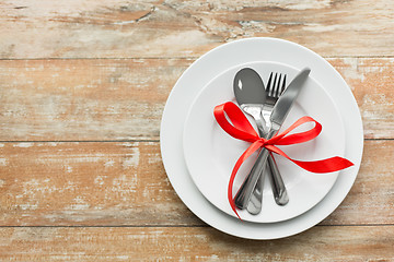 Image showing cutlery tied with red ribbon on set of plates