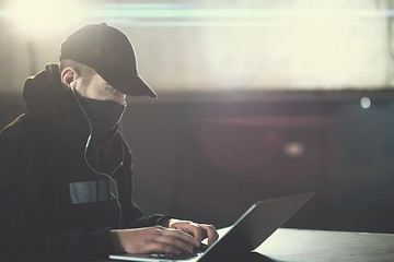 Image showing young talented hacker using laptop computer while working in dar