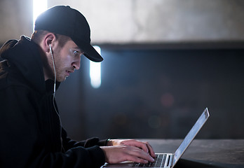 Image showing talented hacker using laptop computer while working in dark offi