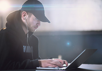 Image showing young talented hacker using laptop computer while working in dar