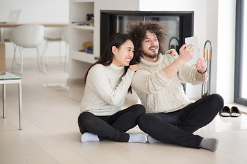 Image showing multiethnic couple using tablet computer in front of fireplace