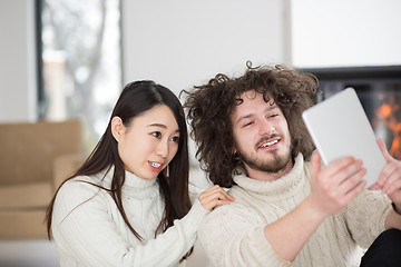 Image showing multiethnic couple using tablet computer in front of fireplace