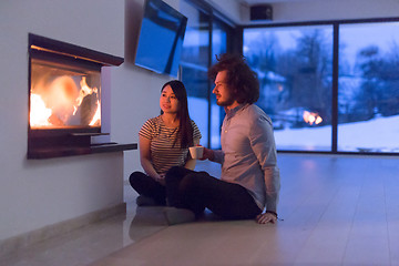 Image showing happy multiethnic couple sitting in front of fireplace