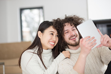 Image showing multiethnic couple using tablet computer in front of fireplace