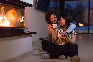 Image showing happy multiethnic couple sitting in front of fireplace