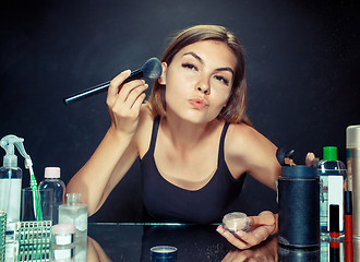 Image showing Beauty woman applying makeup. Beautiful girl looking in the mirror and applying cosmetic with a big brush.