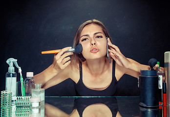 Image showing Beauty woman applying makeup. Beautiful girl looking in the mirror and applying cosmetic with a big brush.