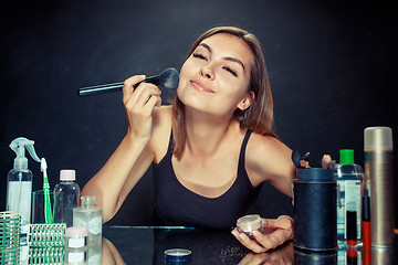 Image showing Beauty woman applying makeup. Beautiful girl looking in the mirror and applying cosmetic with a big brush.