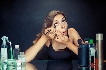 Image showing Beauty woman applying makeup. Beautiful girl looking in the mirror and applying cosmetic with a brush.