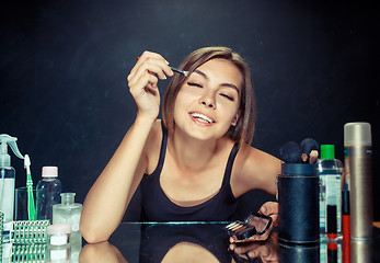 Image showing Beauty woman applying makeup. Beautiful girl looking in the mirror and applying cosmetic with a brush.