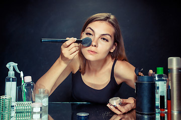 Image showing Beauty woman applying makeup. Beautiful girl looking in the mirror and applying cosmetic with a big brush.