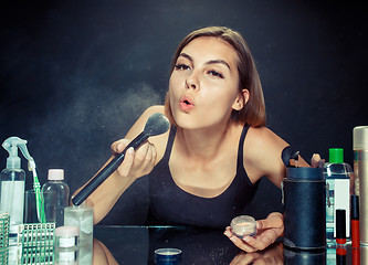 Image showing Beauty woman applying makeup. Beautiful girl looking in the mirror and applying cosmetic with a big brush.