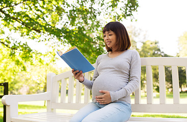 Image showing happy pregnant asian woman reading book at park