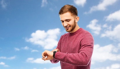 Image showing smiling young man checking time on wristwatch