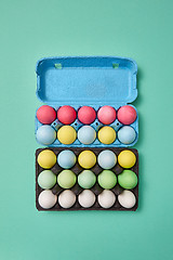 Image showing Multi-colored bright Easter eggs in a blue and black cardboard box on a green background with copy space. Easter layout for your ideas. Flat lay