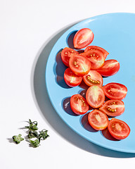 Image showing Halved ripe tomatoes in a blue plate on a gray background with shadows and copy space. Ingredients for salad. Top view