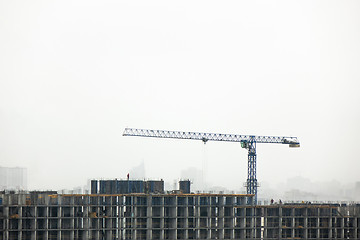 Image showing Construction crane against the cloudy background and the silhouettes of buildings in the misty sky.