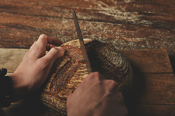 Image showing A man baker cuts bread