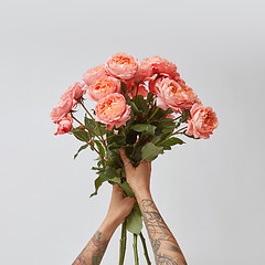 Image showing Girl\'s hands with tattoo hold a bouquet of fresh roses in a color of the year 2019 Living Coral Pantone on a gray background.