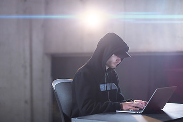 Image showing young talented hacker using laptop computer while working in dar