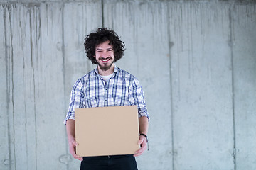 Image showing casual businessman carrying cardboard box in front of a concrete