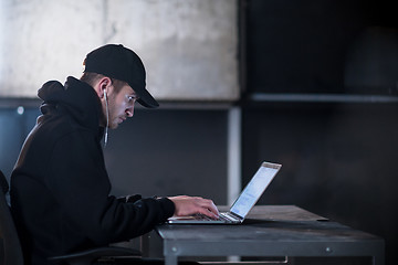 Image showing talented hacker using laptop computer while working in dark offi