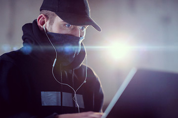 Image showing young talented hacker using laptop computer while working in dar