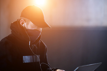 Image showing young talented hacker using laptop computer while working in dar