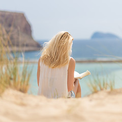 Image showing Woman reading book, enjoying sun on beach.