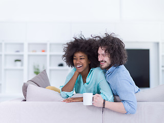 Image showing multiethnic couple sitting on sofa at home drinking coffe