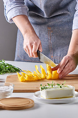 Image showing Woman\'s hands are cutting organic peppers on a wooden board on a gray table. Cooking salad.